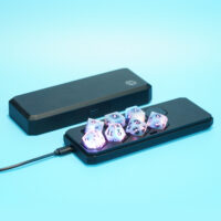 Lit Aurora Sky RPG set placed inside a Large Charging Case with a USB cable plugged into the side of the case.