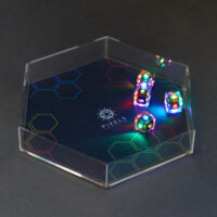 Lit Clear D6s in a hex-shaped clear acrylic dice tray. Tray has a mat with a black and rainbow hex design and Pixels logo in the center.